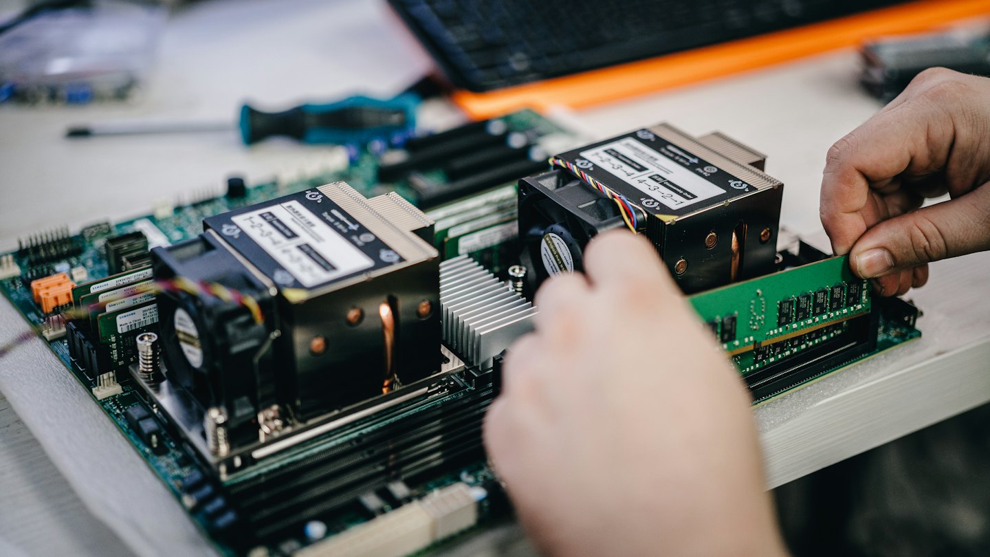 Hands installing a green RAM module into a computer motherboard.