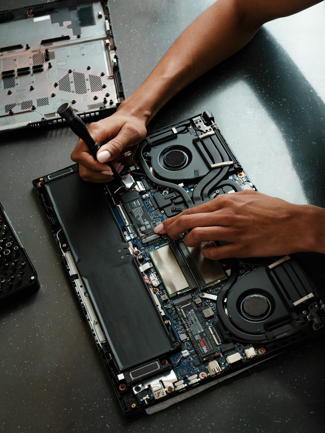 Technician's hands repair open laptop motherboard with tools.